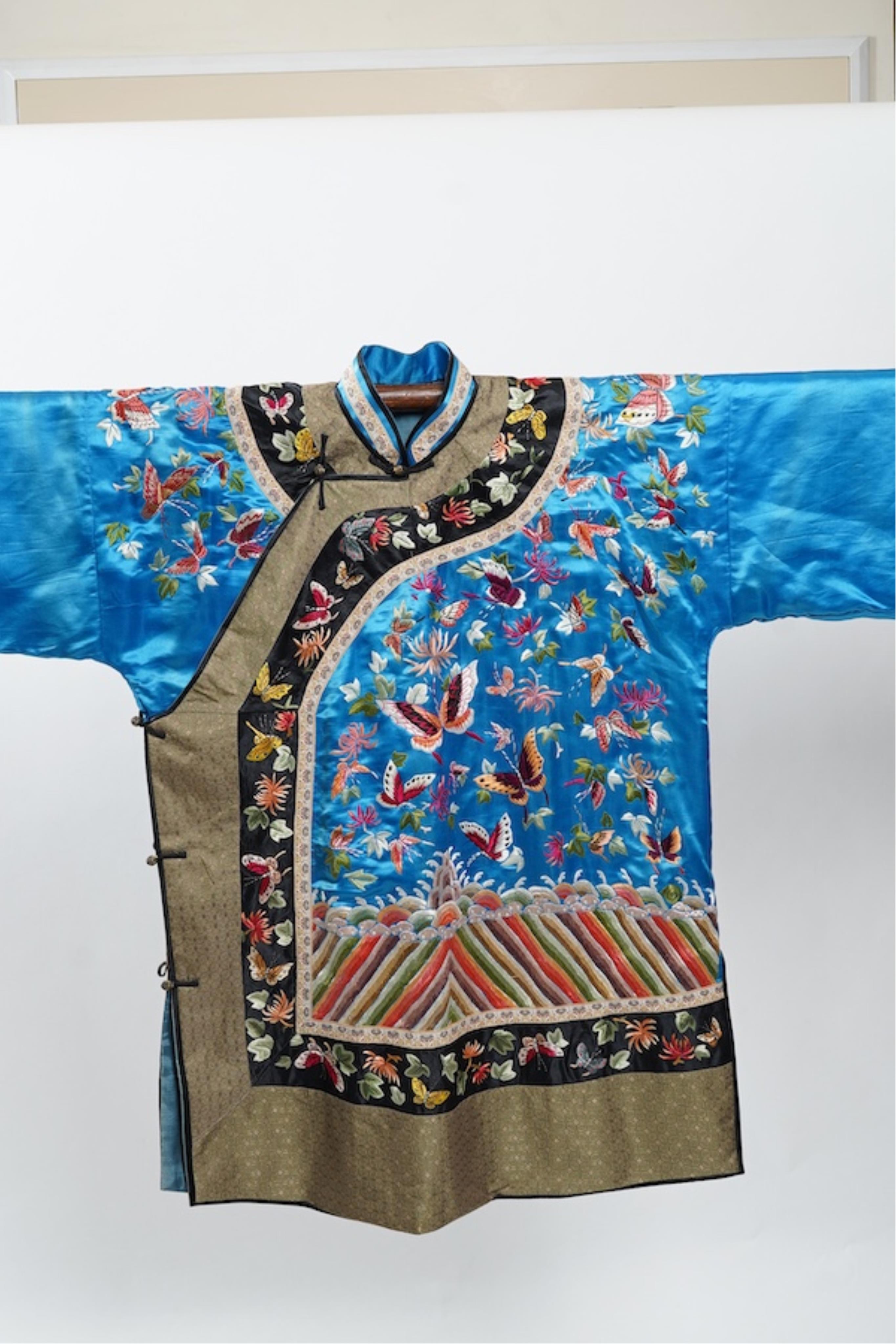 A mid 20th century Chinese turquoise silk jacket, with all over polychrome butterfly embroidery, similar embroidered sleeve bands, front and bottom edges on black silk, all bordered with gold brocade. The jacket blue sil